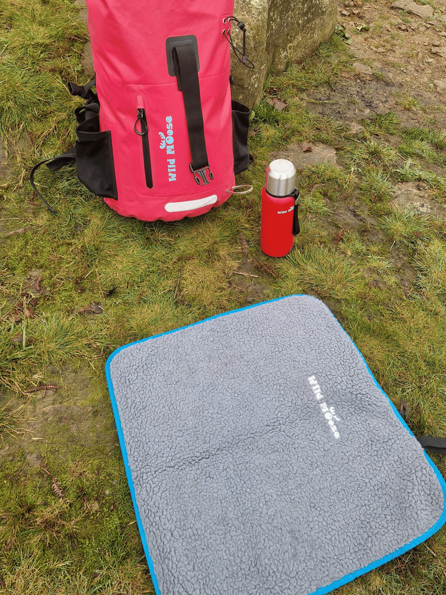 a fleece lined changing mat on grass, with a red flask and pink backpack next to the mat