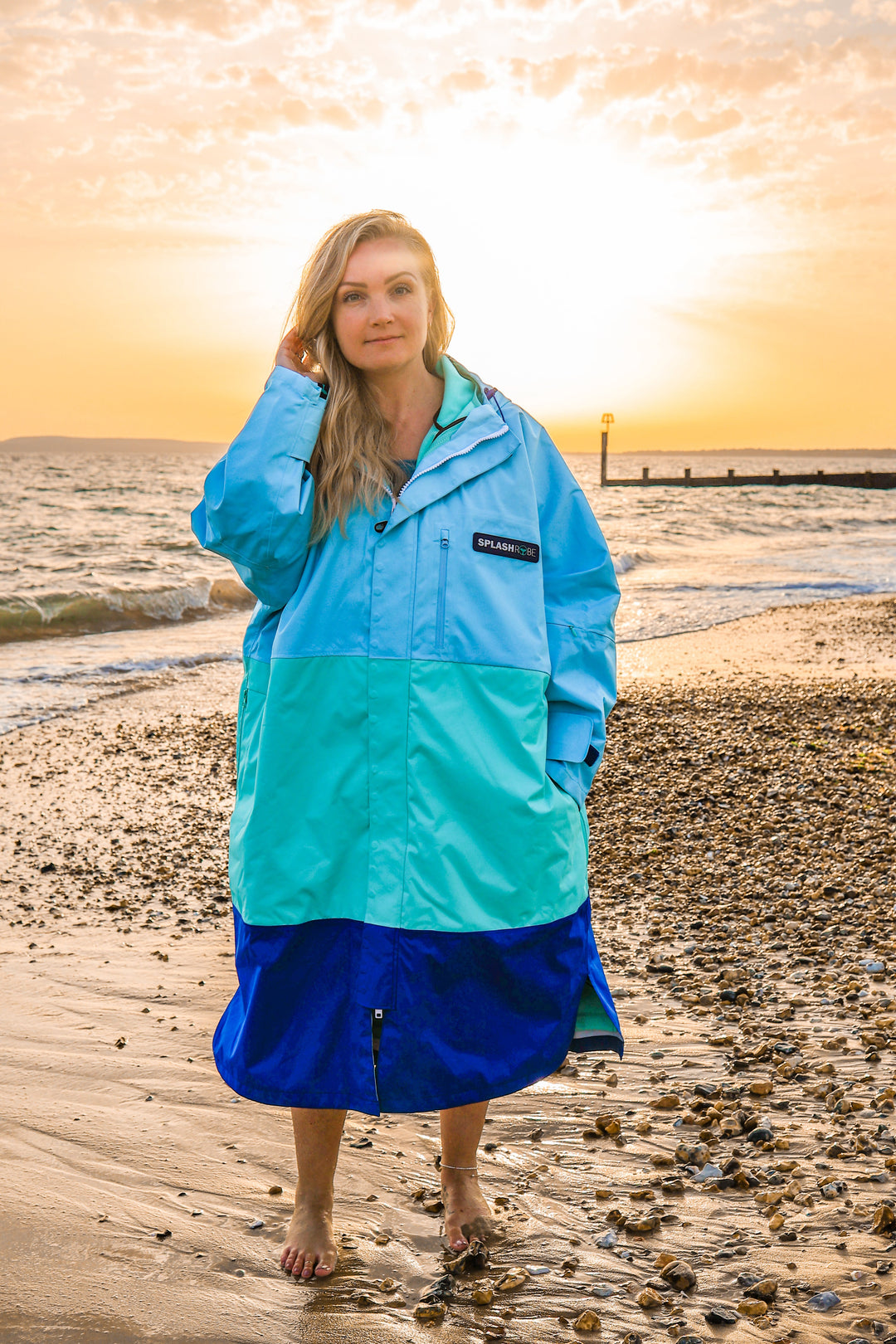 Female wearing the 3 way splashrobe with the sun setting behind her on a beach