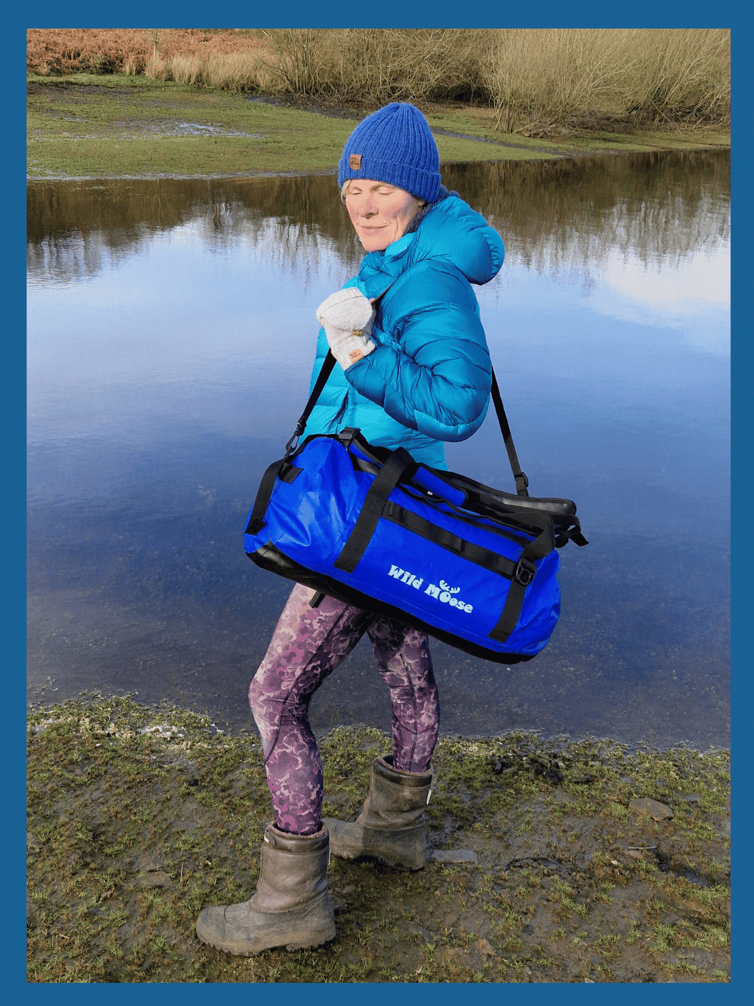 lady stood by water carrying an electric blue duffel bag on her shoulder