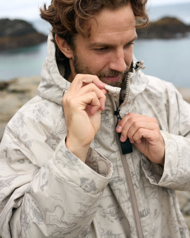 Man zipping a Vivida sherpa weatherproof changing robe Desert Sand by a lake