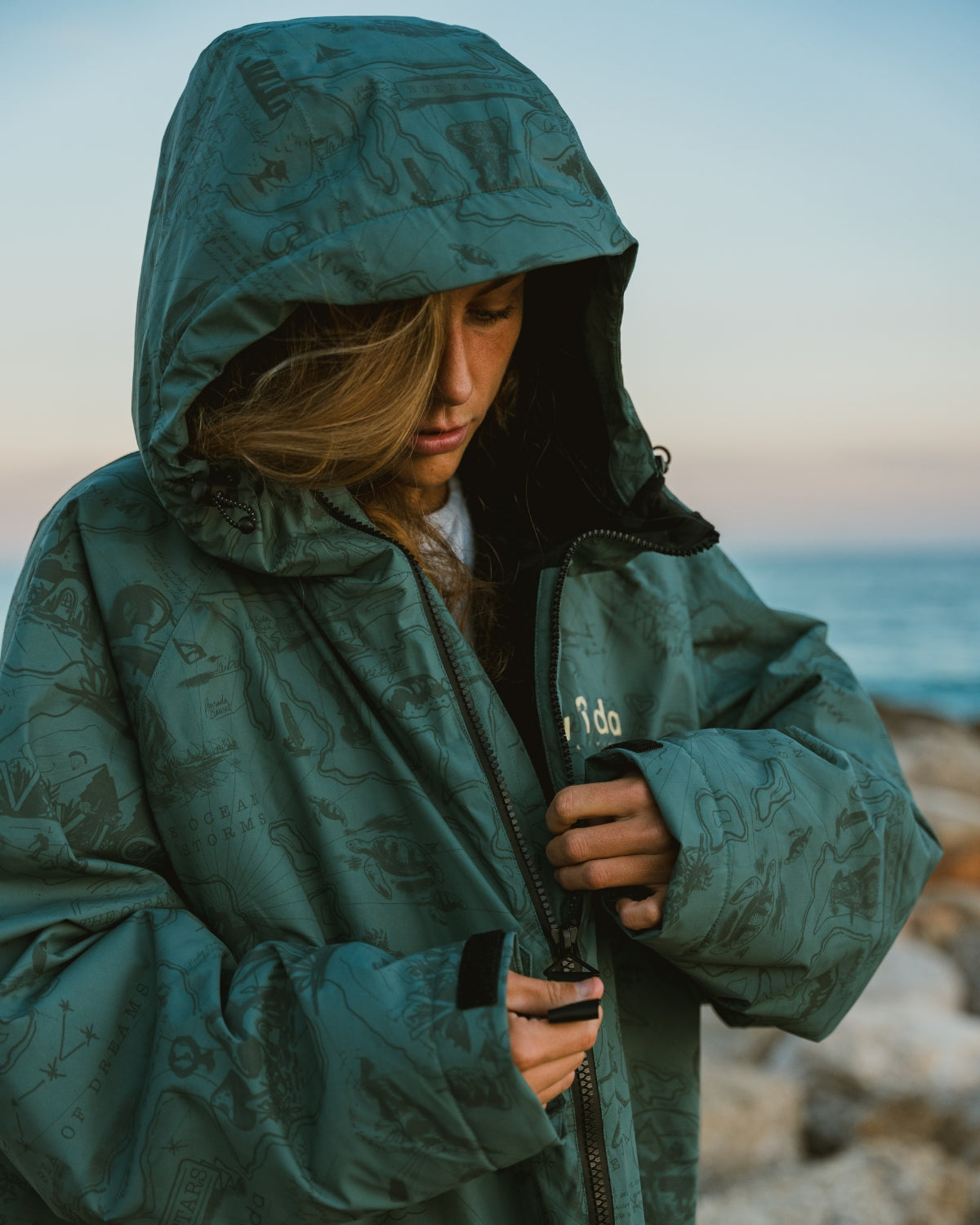 Woman wearing a Vivida sherpa weatherproof changing robe Green Map of Dreams with hood