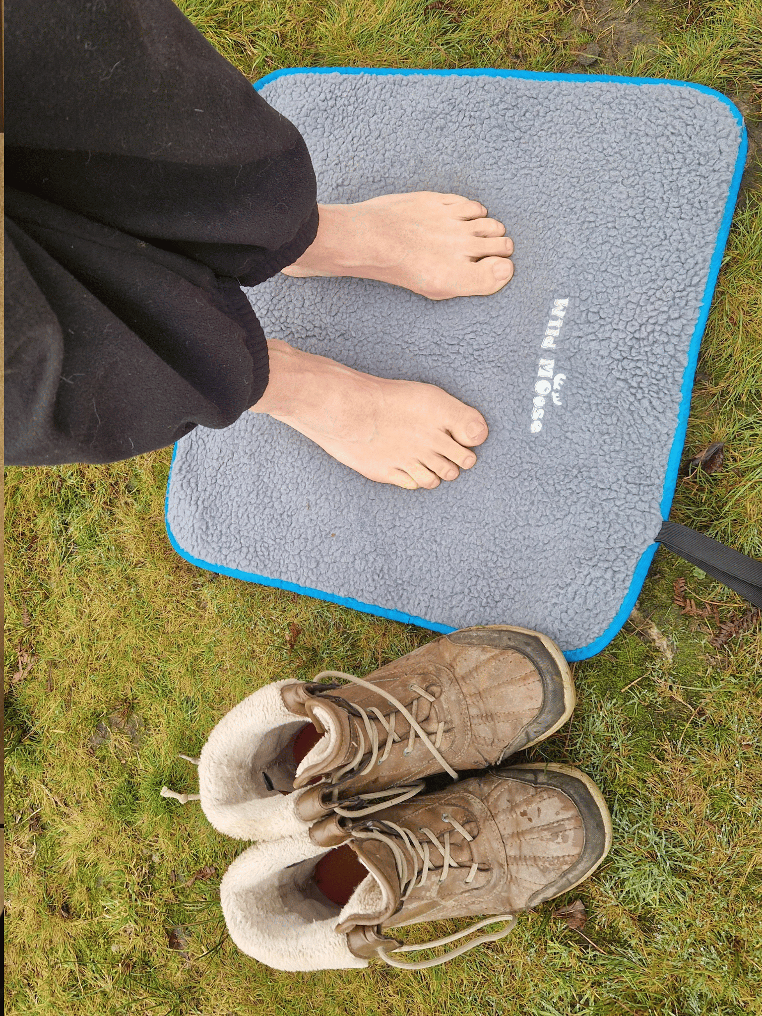 bare feet on a fleece lined changing mat on grass, with a pair of boots next to the mat