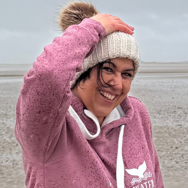 Waves ad Wild Water owner Claire, wears her Winter Swim knitted beanie hat on a very wet and windy beach in South Wales.