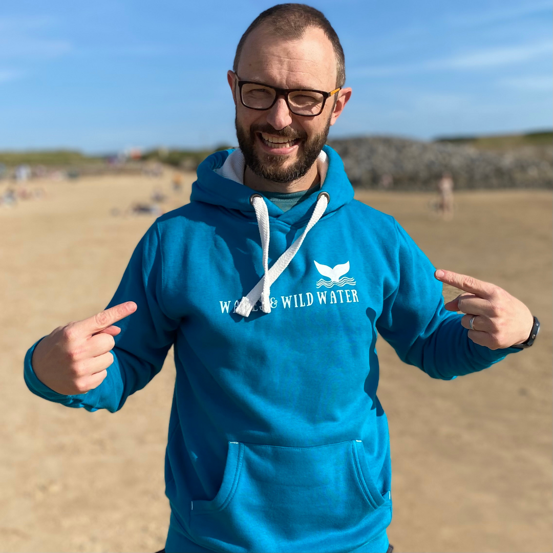 Waves and Wild Water owner Glenn, is enjoying a sunny day on the beach in Wales. Despite the sun, it's a bit chilly, so he's staying warm in his stunning Ocean Depths hoodie. The white logo print across the chest compliments the white inner hood and chunky draw cords.