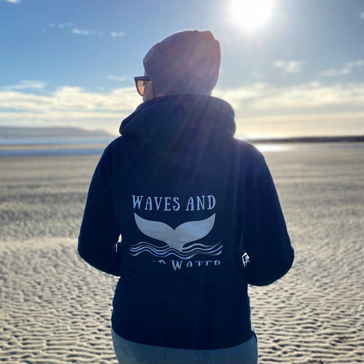 Waves and Wild Water owner, Claire, contemplates the receding tide whilst staying warm in her navy blue snuggly hoodie with the large whale tail logo printed on the back in silver water based ink.